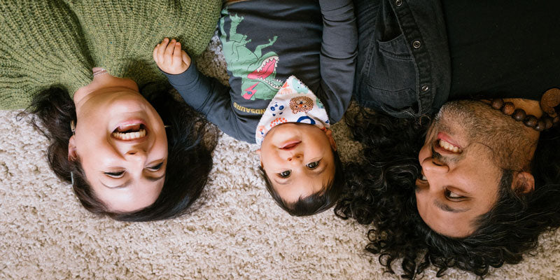 A family lying on the floor with heads touching, smiling at the camera.